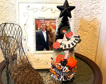 Könnte beinhalten: Ein schwarz-weißer Halloween-Baum mit einem schwarzen Stern oben. Der Baum ist mit einer Papierschnittfigur einer Frau in einem schwarzen Kleid mit schwarzen Katzen und Kürbissen geschmückt. Der Baum steht auf einem Tisch mit einem schwarz-weiß gestreiften Band, auf dem "Halloween" steht.