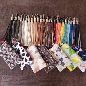 May include: A collection of colourful zippered pouches with various patterns, including floral, geometric, and abstract designs. The pouches are made of fabric and have a tassel zipper pull.