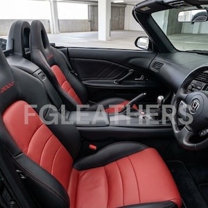 May include: Interior view of a black convertible car with red and black leather seats. The seats have the text "S2000" in red. The steering wheel and dashboard are black. The car is parked in a garage.