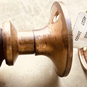May include: A pair of antique brass door knobs with a decorative floral design on one knob. The knobs are attached to a round plate with a screw and a sticker with the numbers 15634868, 4527, and 28650.