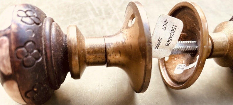 May include: A pair of antique brass door knobs with a decorative floral design on one knob. The knobs are attached to a round plate with a screw and a sticker with the numbers 15634868, 4527, and 28650.