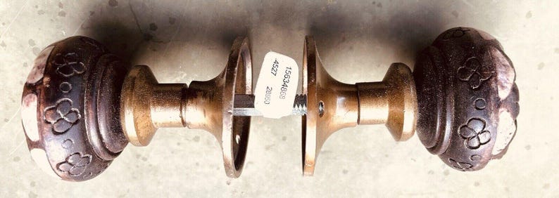 May include: A pair of antique brass door knobs with intricate floral designs. The knobs are attached to a metal rod and have a label with the text "156346W 4527 20000".