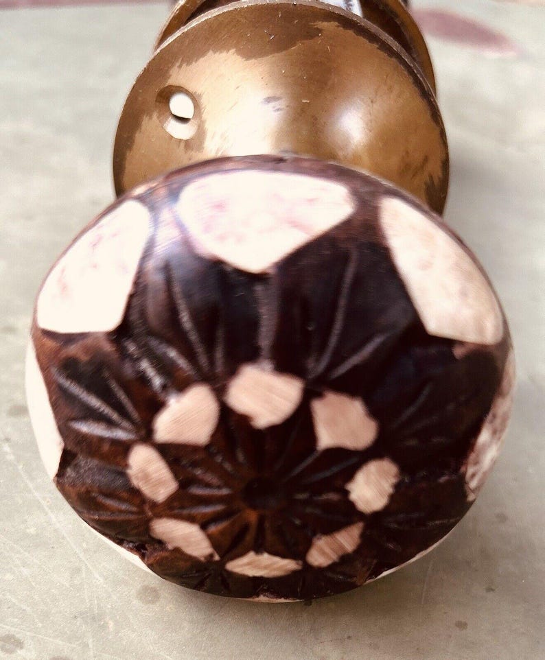 May include: A dark brown wooden door knob with a carved floral design and white accents. The knob is round and has a smooth surface.