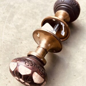 May include: A vintage brass door knob with a dark brown wooden handle. The handle has a floral design with white accents. The knob is attached to a brass backplate.