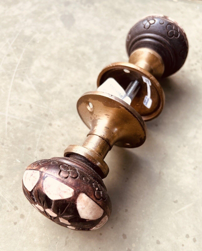 May include: A vintage brass door knob with a dark brown wooden handle. The handle has a floral design with white accents. The knob is attached to a brass backplate.