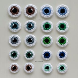 Peut inclure: Une collection de 20 yeux en crochet de différentes couleurs, dont le marron, le bleu, le vert et le gris. Les yeux sont tous de la même taille et de la même forme, et ils sont disposés en quatre rangées de cinq. Les yeux sont faits de fil blanc et ont des pupilles noires.