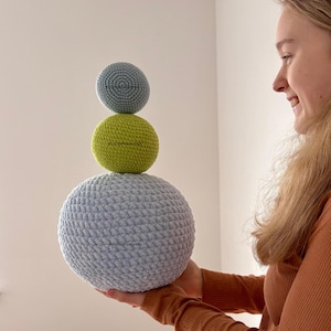 Peut inclure: Une pile de trois boules en crochet, une bleu clair, une verte et une bleu clair. Les boules sont empilées les unes sur les autres, la plus grande en bas et la plus petite en haut. Les boules sont toutes crochetées en point simple.