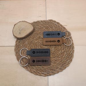 May include: Four leather keychains with metal rings. Each keychain has a different design of a black and white barcode. The keychains are on a brown woven surface.