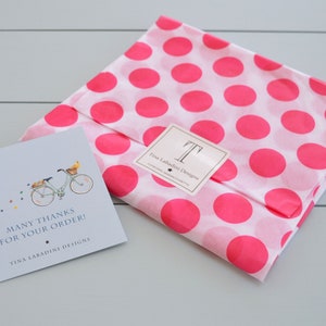 Pu&ograve; includere: Un biglietto di ringraziamento con un'illustrazione di bicicletta e il testo "Many thanks for your order! Tina Laradini Designs". Il biglietto &egrave; su carta velina a pois rosa e bianca.