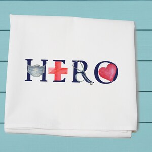 May include: White kitchen towel with the word "HERO" in blue letters. The letters are decorated with a red heart, a red cross, a blue face mask, and a pair of glasses.