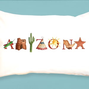 May include: White pillow with the word "Arizona" spelled out in red letters. Each letter is decorated with a different image representing the state, including a chili pepper, a red rock, a cactus, a teepee, a sun, a horseshoe, and a star.