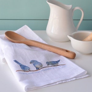 May include: White kitchen towel with a bluebird design and the text "singing sweet songs, of melodies pure and true". A wooden spoon is lying on top of the towel.