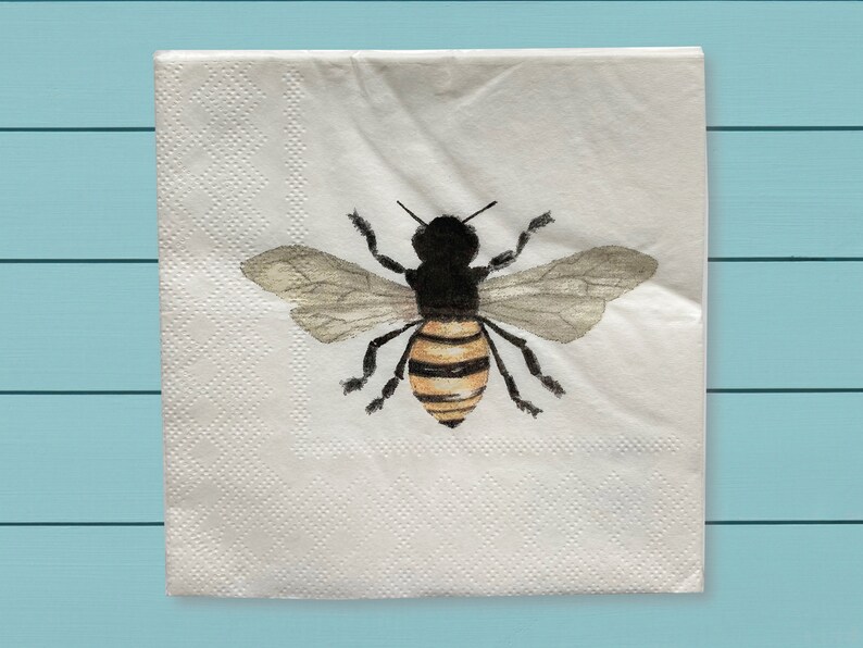 May include: A white paper napkin with a watercolor illustration of a bee. The bee has black and yellow stripes and translucent wings.