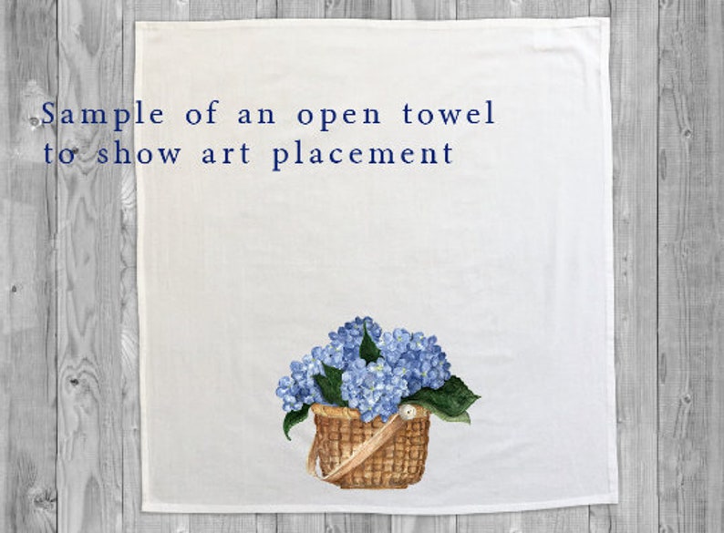 May include: A white kitchen towel with the text "Sample of an open towel to show art placement" printed in blue. A watercolor painting of a basket of blue hydrangeas is centered on the towel.