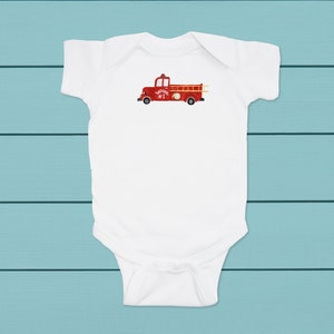 May include: White baby onesie with a red fire truck graphic. The fire truck has a ladder and the words "Ladder Truck #1" on the side.