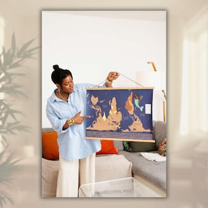 May include: A blue world map with gold foil detailing, displayed on a wooden frame. The map shows continents and countries. The map is being held up by a person.
