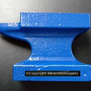 May include: A small blue metal anvil with a rounded top and a flat base. The anvil has a small hole in the side and the text "Copyright Silversmithsupply" is printed on the base.