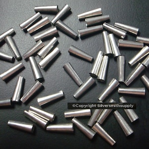 May include: A pile of silver-colored metal cones, scattered on a dark gray surface.  The cones are all the same size and shape, and they are arranged in a random pattern.  Copyright Silversmithsupply.