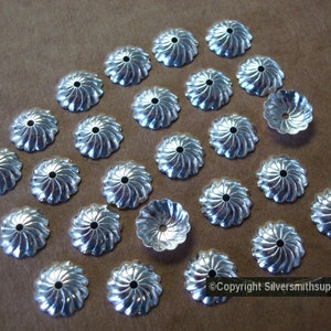 May include: A collection of 25 silver-toned metal bead caps with a swirl design. Some of the caps have a flower-shaped design.