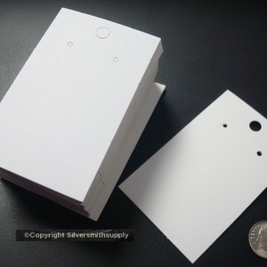 Peut inclure: Une pile de cartes d'affichage pour boucles d'oreilles blanches avec trois trous pour l'affichage des boucles d'oreilles. Les cartes mesurent environ 5 cm sur 7,5 cm.