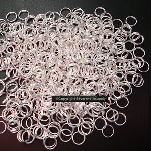 May include: A large pile of silver jump rings. The rings are all the same size and are arranged in a random pattern.  ©Copyright Silversmithsupply