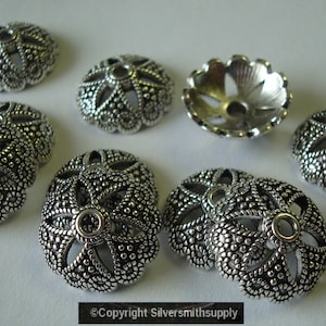 May include: Silver metal bead caps with a decorative floral design. The caps have a small hole in the center for stringing.