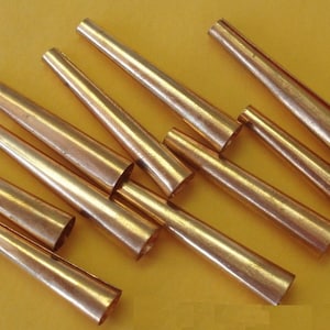May include: A group of 10 copper-colored tapered metal tubes. The tubes are arranged in a random pattern on a yellow surface.