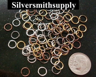 Puede incluir: Un montón de anillos de salto de plata, oro y cobre, con una moneda de 10 céntimos para la escala. Los anillos de salto se utilizan para la fabricación de joyas.