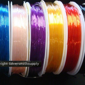 May include: Assortment of 12 spools of clear elastic cord in various colors, including green, black, red, yellow, blue, pink, purple, gold, orange, light blue, teal, and peach. The cord is wound around spools with white plastic.