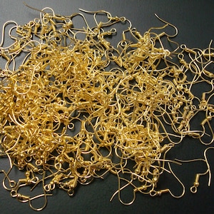 May include: A large pile of gold-colored earring hooks. The hooks are made of metal and have a small loop at the top and a small ball at the bottom.