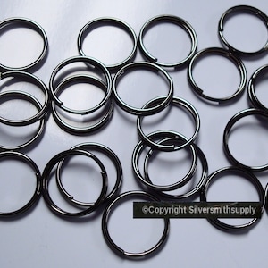 May include: A selection of dark grey metal split key rings, arranged on a white surface. The rings are circular with a split opening for attaching keys or other items. The image is well-lit, showing the metallic sheen of the rings.