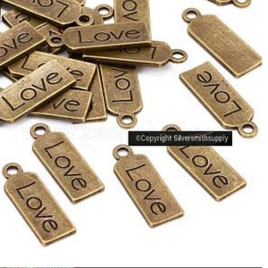 May include: A pile of antique gold-toned metal charms with the word "Love" engraved on them. The charms have a loop at the top for attaching to jewelry or other crafts.