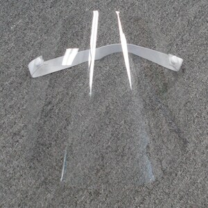 May include: A clear plastic face shield with a white elastic band. The shield is designed to protect the wearer's face from droplets.