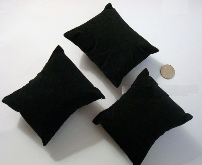 Puede incluir: Tres almohadas de reloj de terciopelo negro, ideales para exhibir relojes u otras joyas. Las almohadas son cuadradas y tienen una textura suave y mullida.
