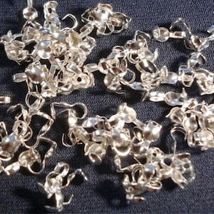 May include: A pile of silver-toned metal clasps with a loop on one end and a small ball on the other end. The clasps are used for jewelry making.