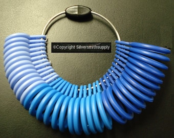Può includere: Uno strumento per misurare la taglia dell'anello con un anello di metallo che tiene una serie di anelli di plastica blu e blu chiaro. Gli anelli sono numerati e possono essere utilizzati per determinare la taglia dell'anello corretta.