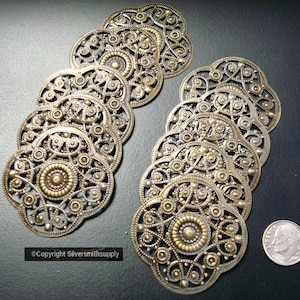 May include: A set of 10 gold-toned metal filigree embellishments with intricate designs. The embellishments are circular and have a raised center with a smaller circle. The embellishments are perfect for adding a touch of elegance to any craft project.