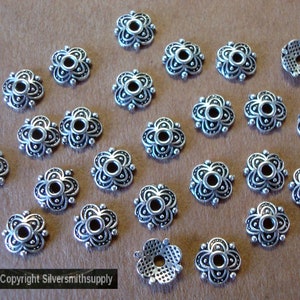 May include: Twenty-two silver-toned metal flower-shaped bead caps with a hole in the center. The bead caps have a decorative design.
