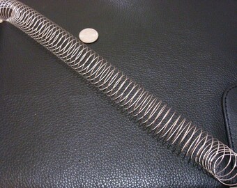 May include: A silver metal spring coil, about 10 inches long, is lying on a black leather surface. A silver coin is visible in the background.