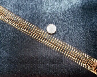 May include: A gold-colored metal spring coil on a black leather surface. A silver coin is next to the spring.