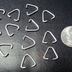 May include: A close-up of a group of silver triangle jump rings. The rings are about the size of a dime.
