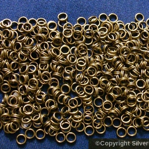 May include: A large quantity of small, gold-coloured jump rings. The rings are all the same size and are arranged in a random pattern.
