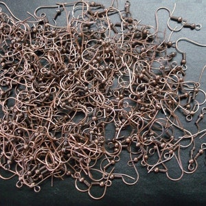 May include: A large pile of copper-colored earring hooks. The hooks are all the same size and shape, and they are arranged in a random pattern.