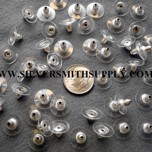 May include: A close-up of a pile of silver earring backs with clear plastic backs. The backs are designed to be used with post earrings.