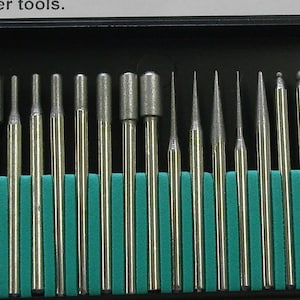 May include: A set of 25 silver diamond burrs in a black plastic case with a teal blue foam insert. The burrs are arranged in rows and are of various shapes and sizes.