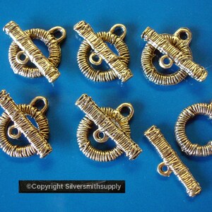 May include: Seven gold-toned metal clasps, each with a circular design and a bar across the center. The clasps are designed for use in jewelry making.