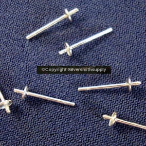 May include: Six silver earring posts with flat backs. The posts are arranged on a blue fabric surface.