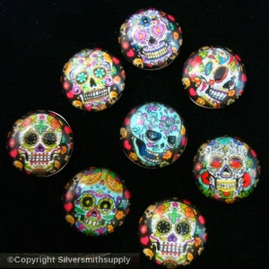 May include: Nine colorful glass cabochons with images of sugar skulls, a traditional Mexican symbol of Day of the Dead. The skulls are decorated with flowers, hearts, and other patterns.