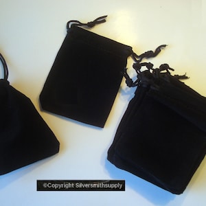 May include: Several black velvet drawstring pouches of varying sizes are displayed against a white background. The pouches are closed with black cords. The image is well-lit, highlighting the texture and shape of the pouches.