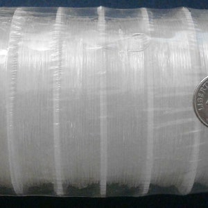 May include: A roll of clear fishing line wrapped around a cardboard tube. The line is packaged in plastic wrap and a dime is placed on the roll for size comparison.